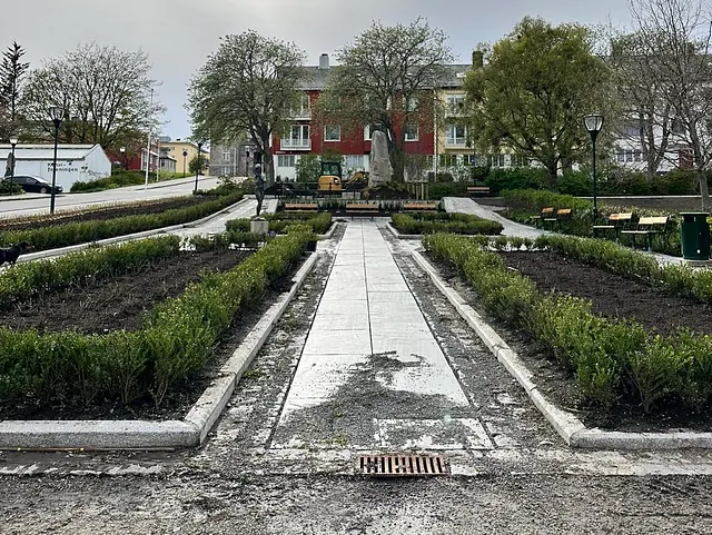 Symmetrisk park med nyanlagte gangstier, benker, grøntarealer og statue i midten.