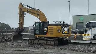 Gul CAT gravemaskin med Mekvik logo løfter stein og grus over i lastebil