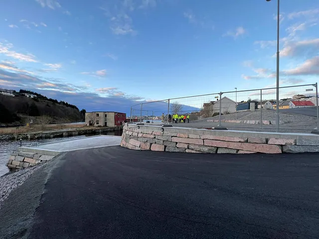 Nytt kaiområde ferdigstilt med steinmurer og asfaltdekke. Arbeidere i bakgrunnen klargjør området for åpning eller overlevering.