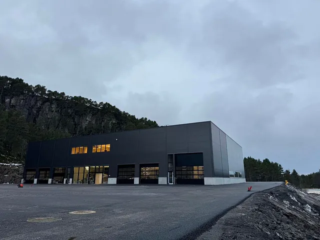 Moderne industribygg med svart fasade og store porter, omgitt av nyasfaltert uteområde.