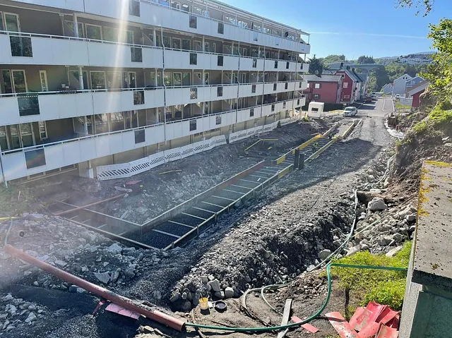 Grunnarbeid og oppbygging av nytt gangfelt eller fortau foran boligblokk pågår, med ferdige forskalingsrammer på plass.