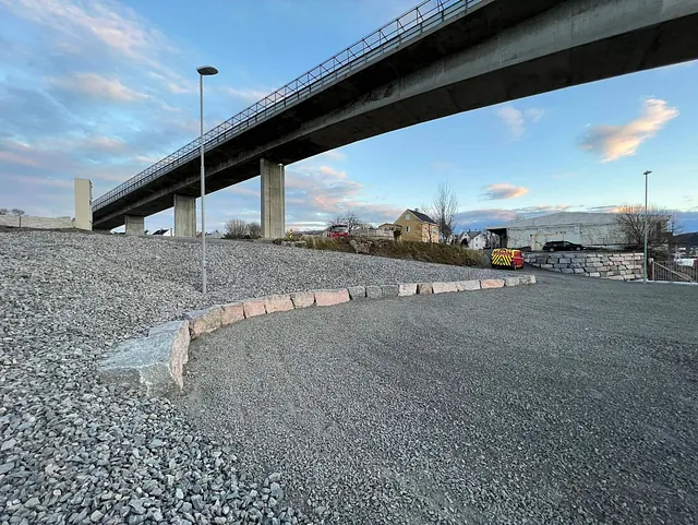 Gruslagt område under bru med granittkantstein og gatebelysning under anleggsutvikling.