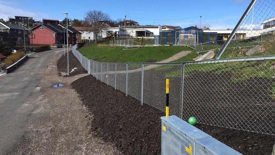 Nytt gjerde satt opp langs gangvei i boligområde med nylagt jord og byggeplass i bakgrunnen.