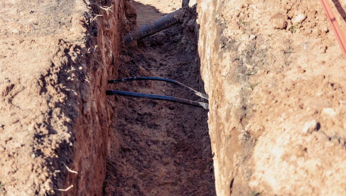 Ledninger og rør er synlige i grop gravd i jord