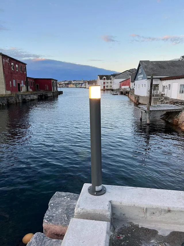 Nytt bryggeområde med lyktestolpe og utsikt over sjø og eldre sjøboder i kveldssol.