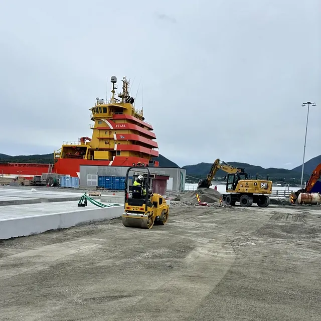Veiarbeid på kaiområde med rullekomprimering og gravemaskin, og supplyskip liggende ved kaien.