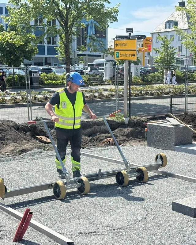 Arbeider jevner ut underlag med spesialverktøy før legging av steinheller i sentrumsområde.