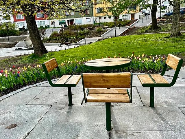 Parkbord med benker foran blomstrende tulipaner og trær, omgitt av grønt gress og trapper.