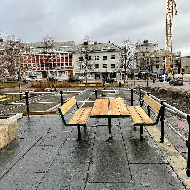 Uteplass med benker og bord i park, med bygårder og byggeaktivitet i bakgrunnen.