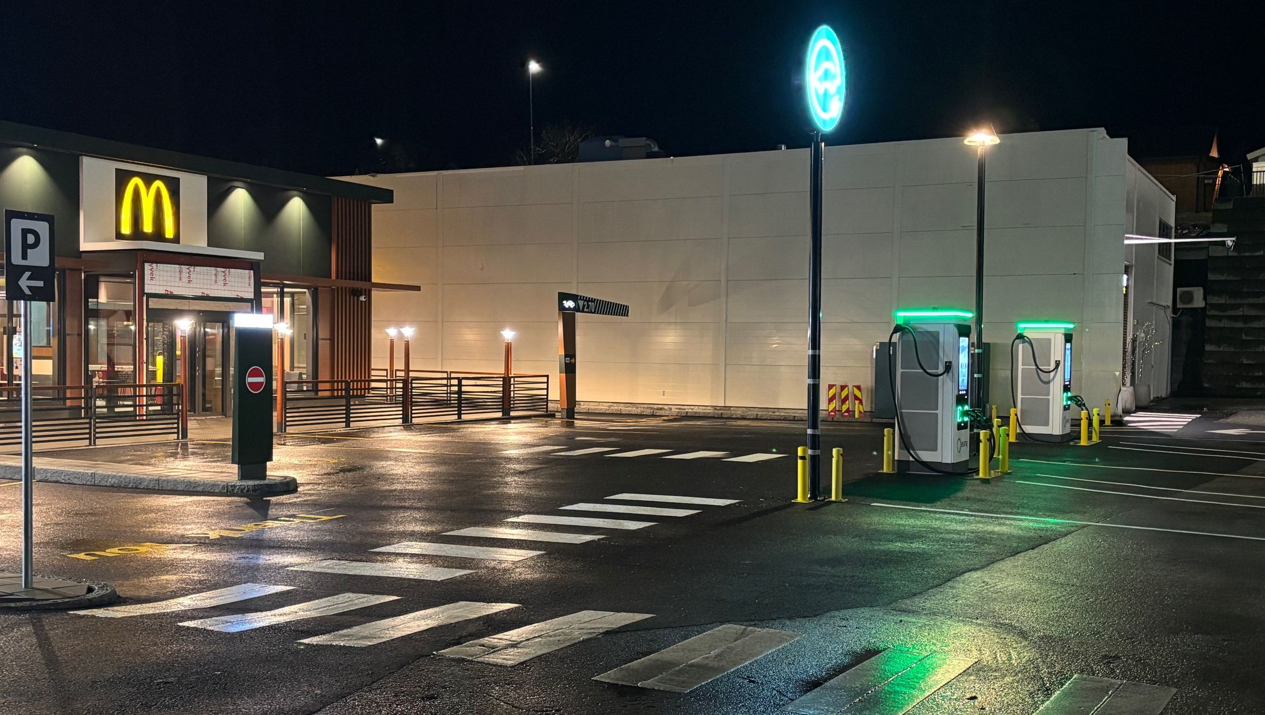 Gravemaskin arbeider med utgraving nær et inngjerdet lekeområde i et boligområde med hus og trær i bakgrunnen.