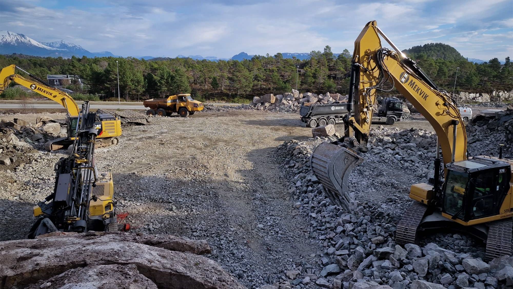Gravemaskiner med Mekvik logo i arbeid på anleggsområde med masse stein