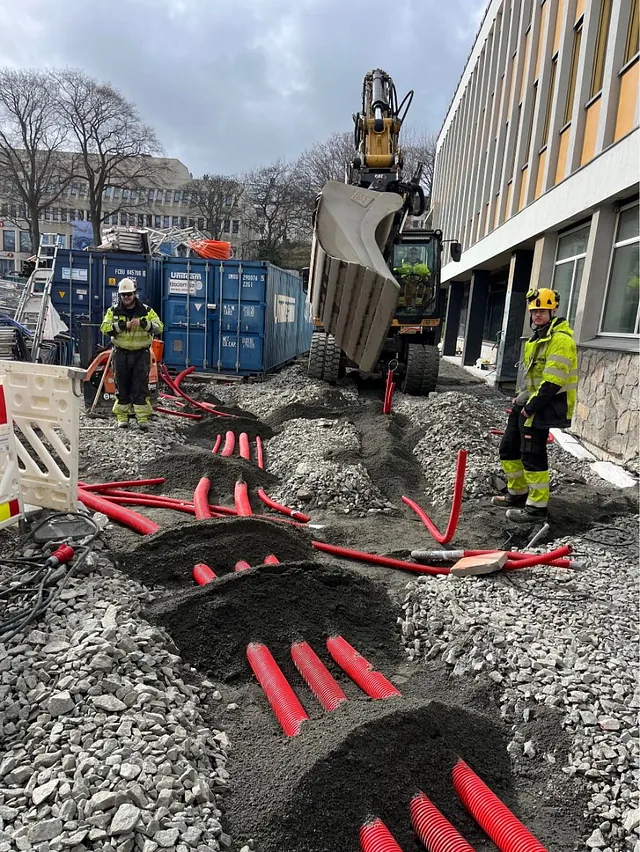 Legging av trekkerør og grøftearbeid ved bygg, med omfattende kabelføringer og maskinbruk.